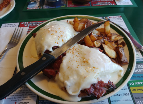 A plate of biscuits and gravy topped with meat, served with golden-brown home fries and a knife on the side.