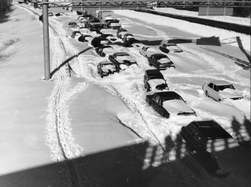 A snow-covered highway with stranded cars buried in deep snow, creating a traffic jam in winter conditions.
