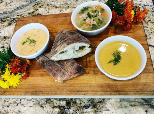 A wooden board with two bowls of soup, a piece of bread, and garnished with colorful flowers.