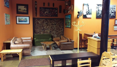 Cozy café interior with orange walls, eclectic seating, wooden tables, and decorative art on the walls.