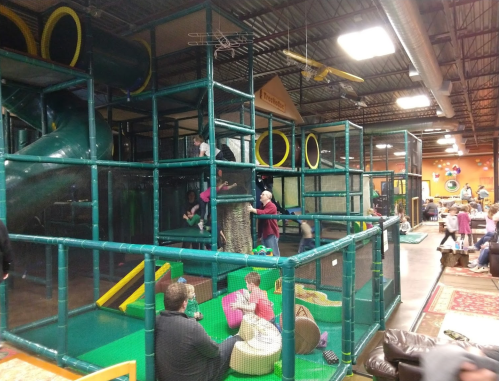 A colorful indoor play structure with children climbing, sliding, and playing in a spacious recreational area.