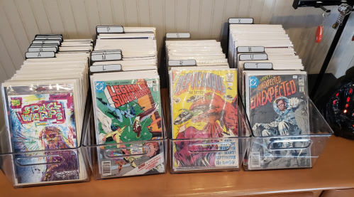 A display of comic books in clear bins, organized alphabetically, featuring colorful covers and titles.
