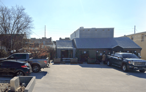 A small building with a metal roof, surrounded by parked trucks, under a clear blue sky. Snowflake decorations are visible.