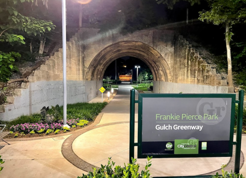 A pathway leading through an archway at Frankie Pierce Park, with a sign for Gulch Greenway and lush greenery around.