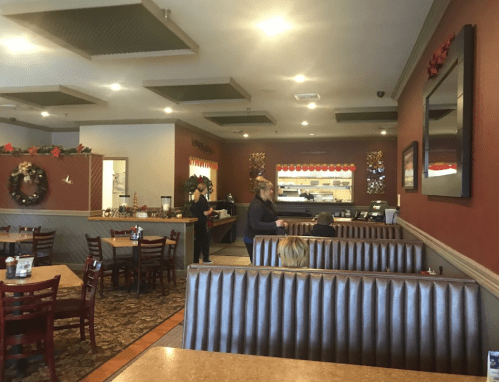 A cozy restaurant interior with festive decorations, featuring booths and a counter area. Customers are seated and staff is serving.