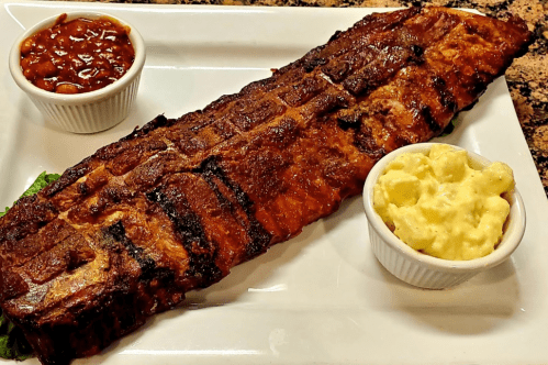 A large grilled rib rack served on a plate with sides of baked beans and creamy macaroni salad.
