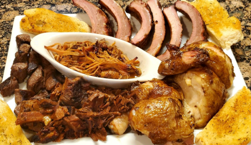 A platter of assorted meats including sliced brisket, pulled pork, chicken, and toasted bread.