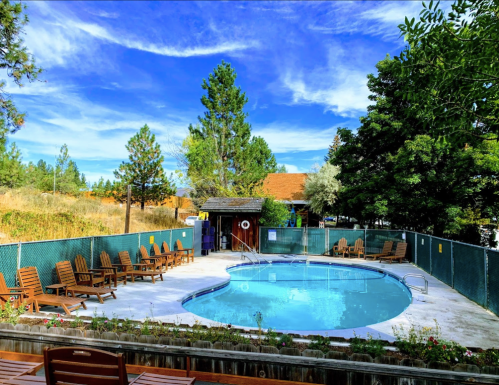 A serene outdoor pool area surrounded by trees and lounge chairs under a blue sky with fluffy clouds.
