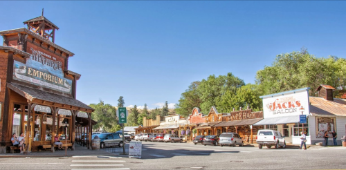 A charming western-style street with wooden buildings, shops, and parked cars under a clear blue sky.