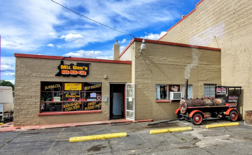 Exterior of Miz Dee's BBQ restaurant with a smoker outside, blue sky, and clouds in the background.