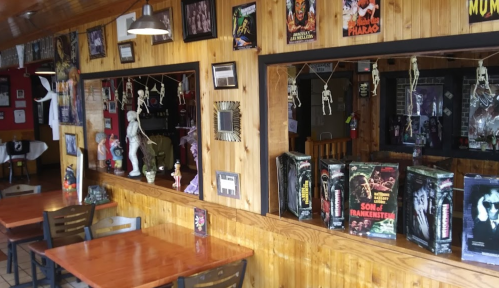 Interior of a themed restaurant with wooden walls, horror movie posters, and skeleton decorations. Tables are set for dining.
