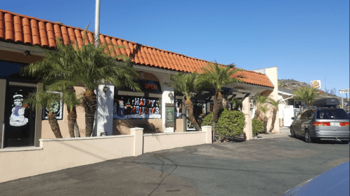A colorful restaurant exterior with palm trees, an "OPEN" sign, and festive window decorations on a sunny day.