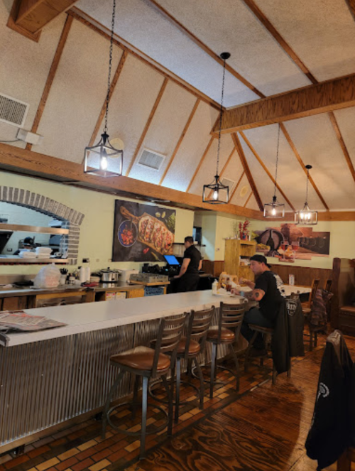 Interior of a cozy restaurant with wooden beams, a bar area, and a chef preparing food in the background.