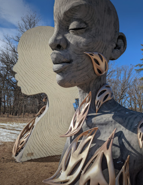 A large, abstract sculpture of a woman's face with intricate, metallic details and a silhouette in the background.