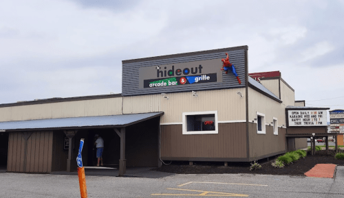 A building with a sign reading "The Hideout Arcade Bar & Grille," featuring a Spider-Man figure on the exterior.
