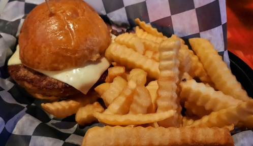 A juicy burger with melted cheese on a toasted bun, served with crispy crinkle-cut fries on a checkered plate.