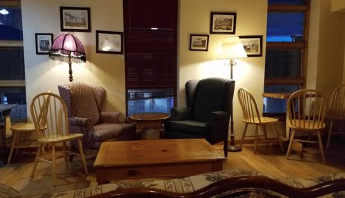 Cozy living area with two armchairs, a coffee table, and several wooden chairs, illuminated by lamps.