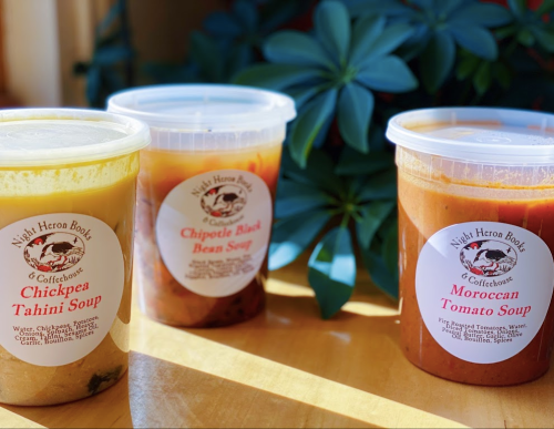 Three soup containers labeled Chickpea Tahini, Chipotle Black Bean, and Moroccan Tomato, with a plant in the background.