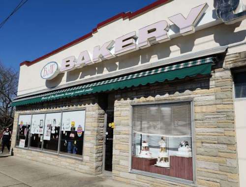 A bakery storefront with a green awning, displaying cakes in the windows and colorful decorations on the walls.