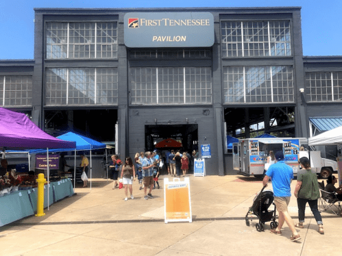 Entrance to the First Tennessee Pavilion, bustling with visitors and colorful tents for an event or market.