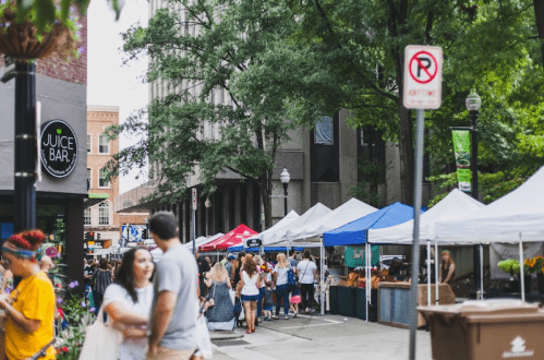 A bustling street market with colorful tents, people walking, and a juice bar sign in the foreground.