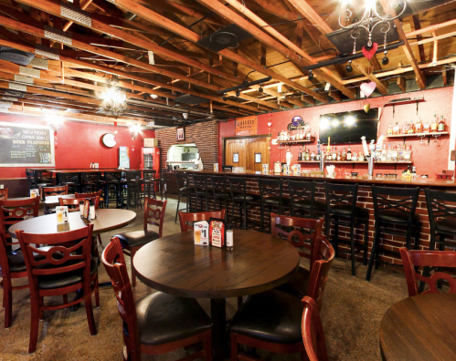 Interior of a cozy restaurant with wooden tables, a bar area, and exposed beams, featuring red walls and a warm atmosphere.