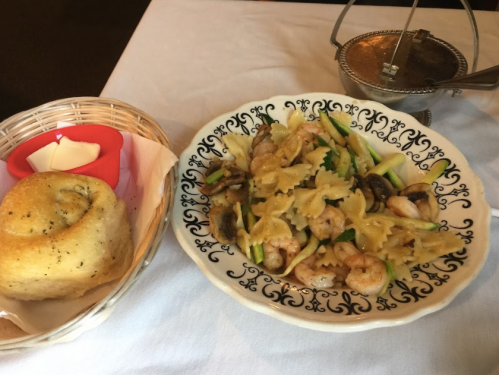 A plate of shrimp pasta with vegetables, accompanied by a roll and a small dish of butter.