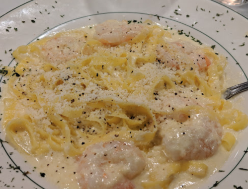 A plate of fettuccine pasta with shrimp in a creamy sauce, garnished with herbs and grated cheese.