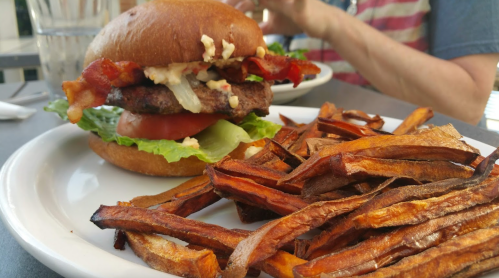 A juicy burger with bacon, lettuce, tomato, and sauce, served with a side of crispy sweet potato fries.