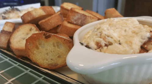 A close-up of a dish with creamy baked dip and toasted bread slices on a platter.