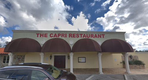 Exterior of The Capri Restaurant featuring a sign, arched awnings, and a cloudy sky in the background.