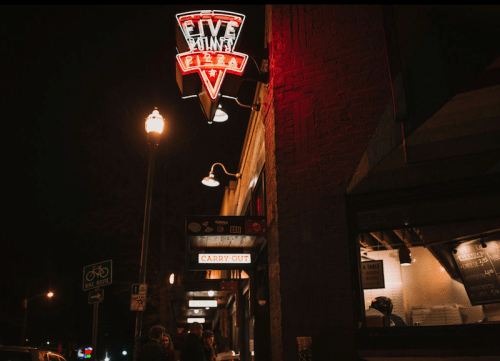 Neon sign for "Five Points Pizza" illuminated at night, with a carry-out window visible.
