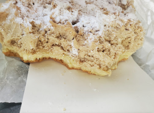 A close-up of a crumbly, powdered sugar-topped dessert on a white paper plate.
