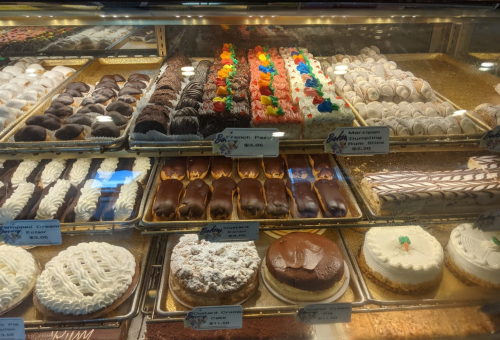 A display case filled with various pastries and cakes, including cream-filled treats and colorful frosted desserts.