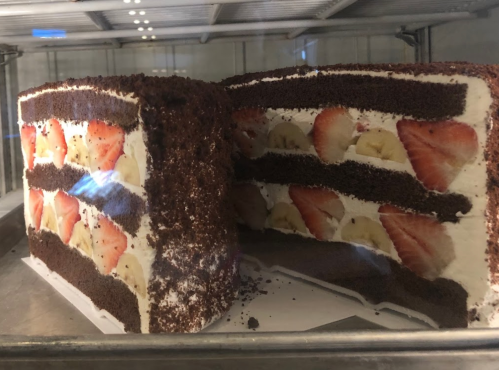 A layered cake with chocolate, strawberries, and bananas, displayed in a glass case.