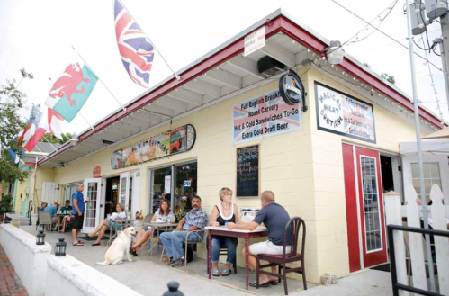 A casual eatery with outdoor seating, flags displayed, and patrons enjoying food and drinks on a sunny day.