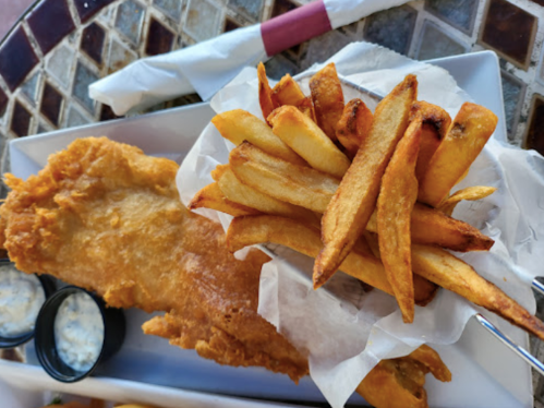 A plate of golden fried fish next to a serving of crispy French fries, with dipping sauces on the side.