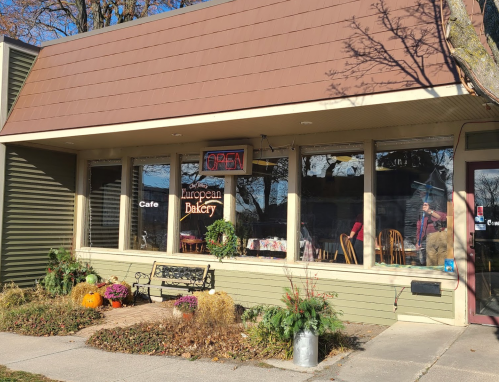 A cozy bakery with a "Open" sign, featuring outdoor seating and autumn decorations.