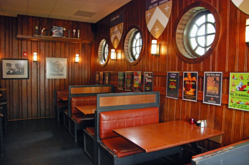 Cozy restaurant interior with wooden walls, circular windows, and booths adorned with colorful posters.