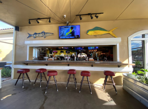 A bar area with red stools, a TV on the wall, and colorful fish decorations in a bright, open space.