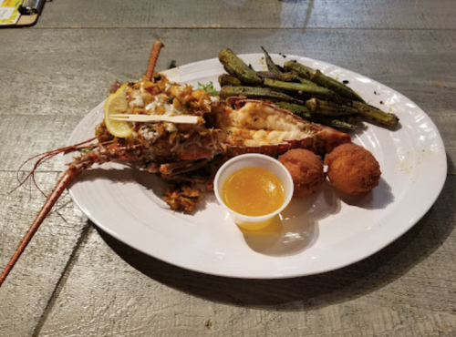 A plate featuring stuffed lobster, fried balls, and grilled green beans, served with a small cup of sauce.
