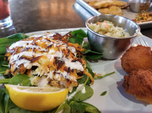 A plate featuring a crab cake salad with spinach, lemon, and a side of coleslaw, alongside two fried balls.