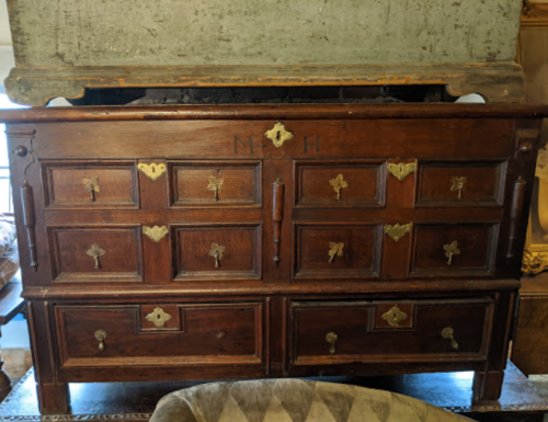 A vintage wooden chest of drawers with multiple compartments and brass handles, featuring engraved initials "M H."