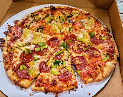 A pizza with pepperoni, green peppers, and artichokes, partially sliced, in a pizza box.