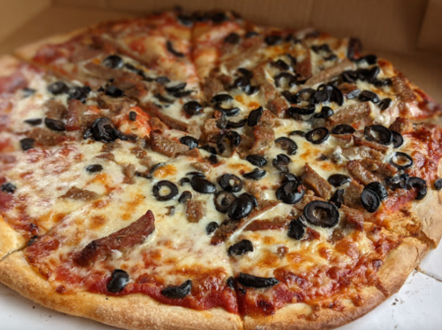 A pizza topped with cheese, black olives, and slices of meat, presented in a pizza box.