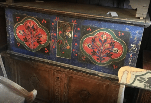 A vintage wooden chest with colorful floral designs in red, green, and blue, set in a rustic interior.