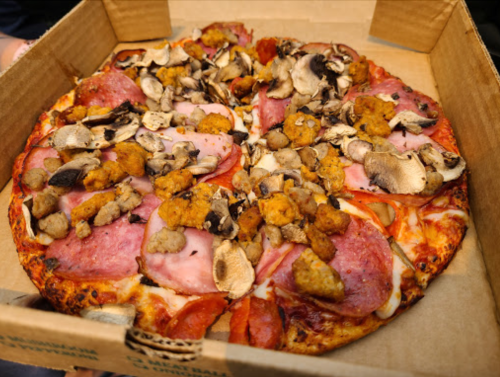 A pizza topped with pepperoni, ham, mushrooms, and sausage in a cardboard box.