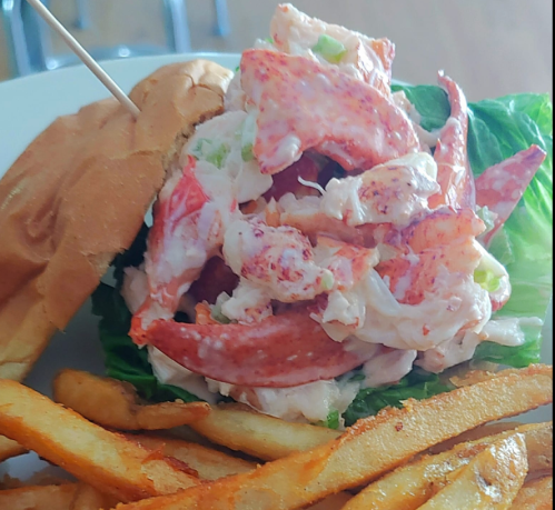 A lobster roll filled with lobster meat and lettuce, served with a side of golden French fries.