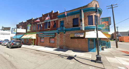 A brick building with colorful awnings and flags, housing a restaurant, located on a city street.