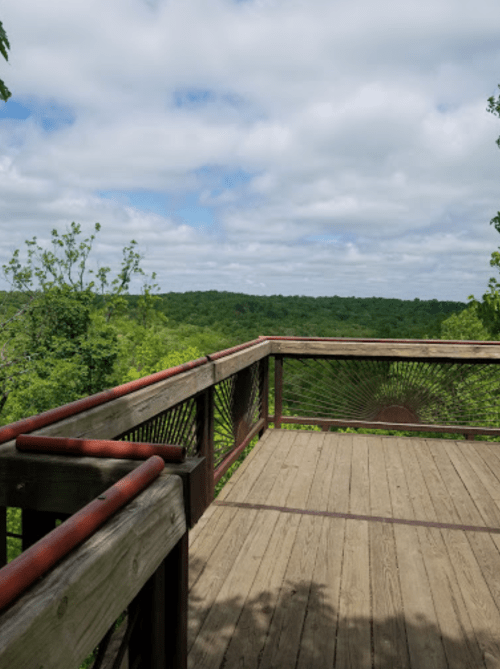 View from a wooden observation deck overlooking a lush green landscape under a cloudy sky.